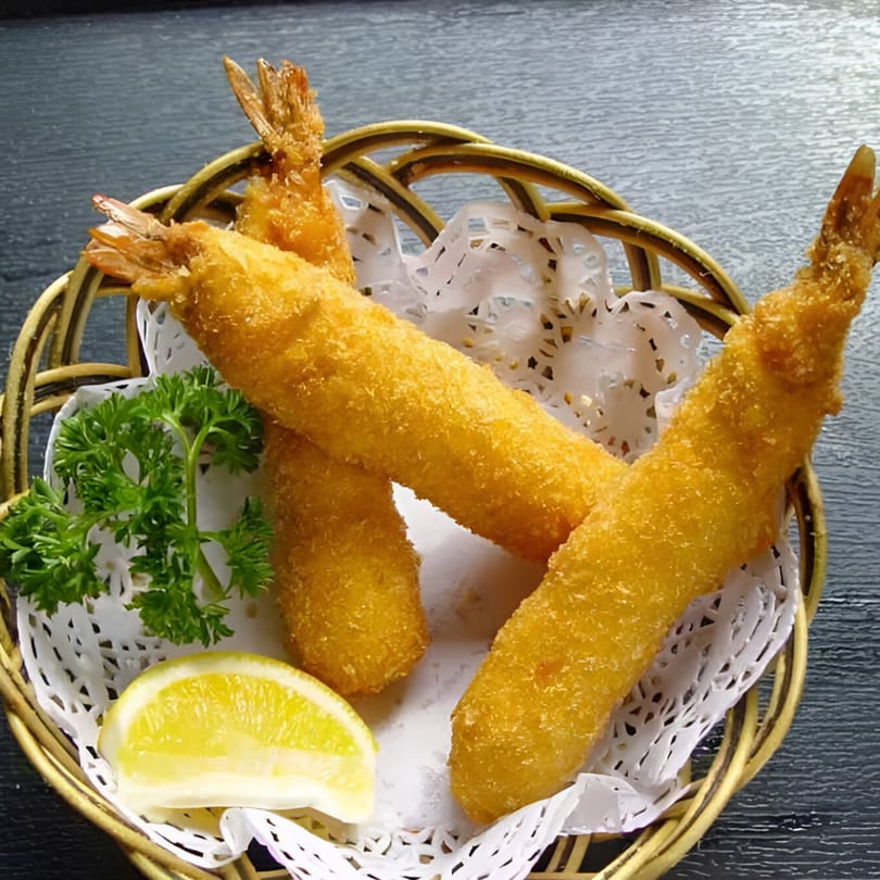 Golden fried shrimp tempura with a lemon wedge and parsley in a woven basket.