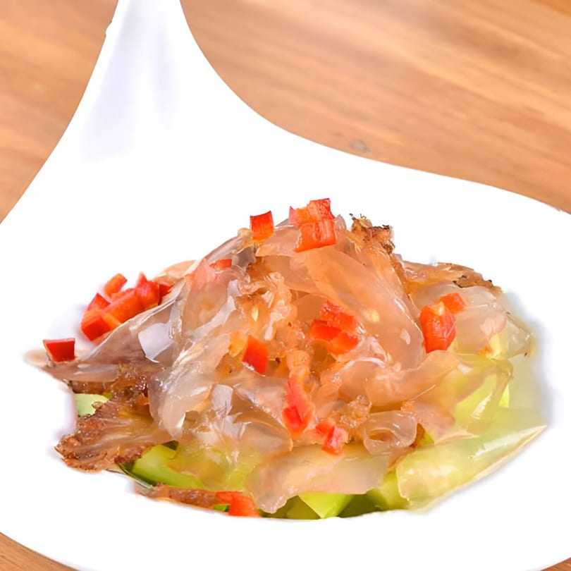 Bo Loong's jellyfish salad with red peppers and cucumber in a white bowl on a wooden table.